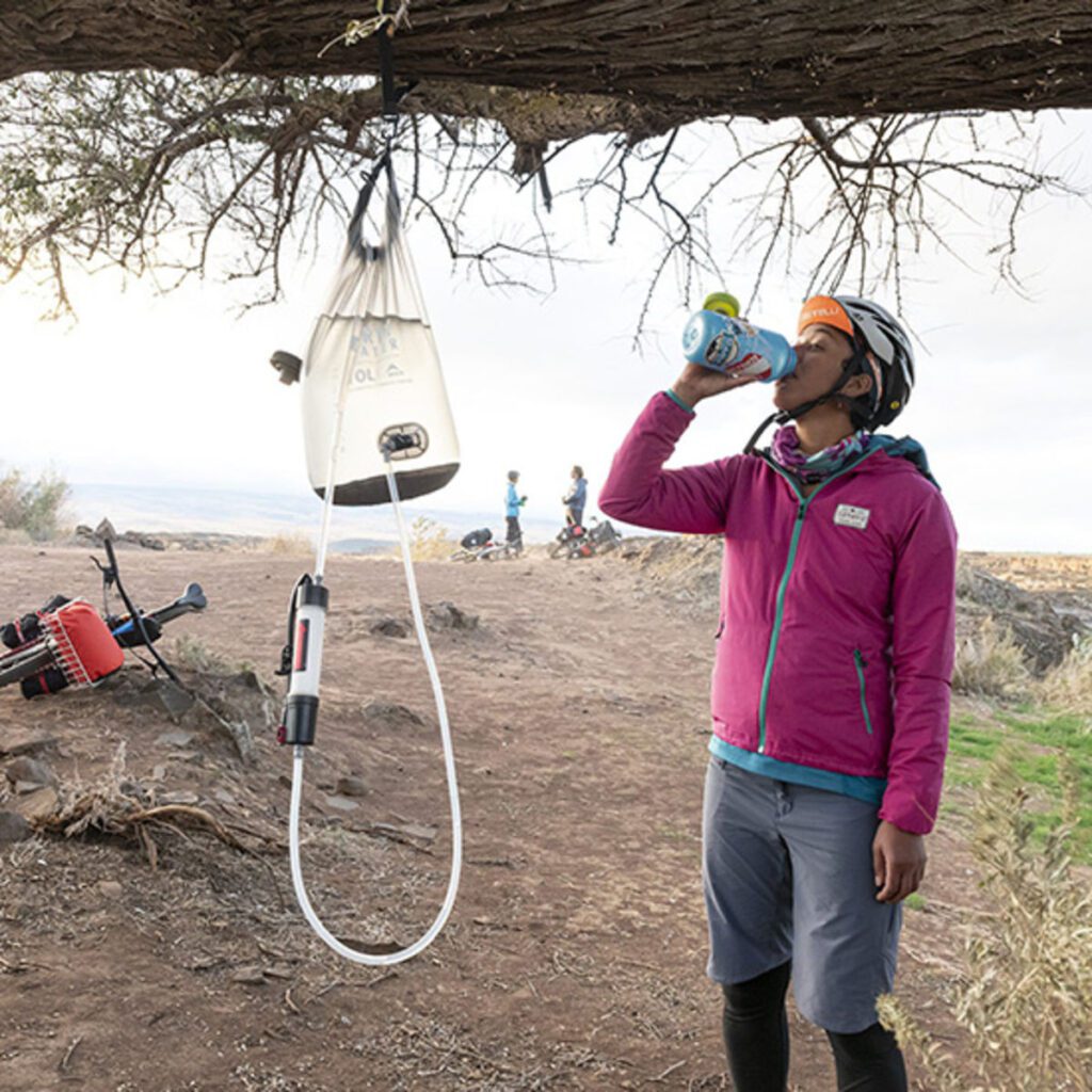 femme boit de l'eau purifiée avec un purificateur suspendu en camping