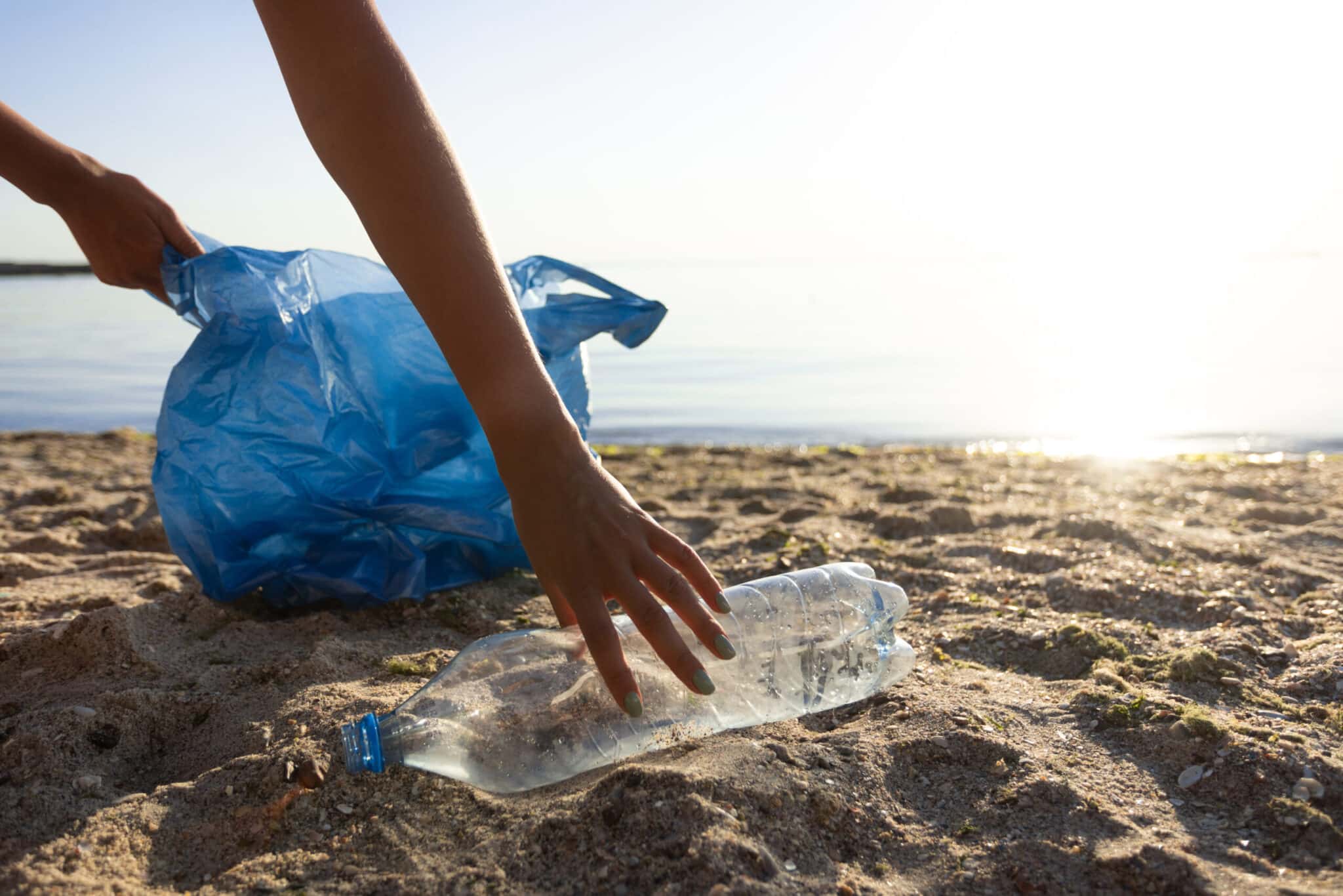 Main qui ramasse une bouteille en plastique sur la plage pour la jeter