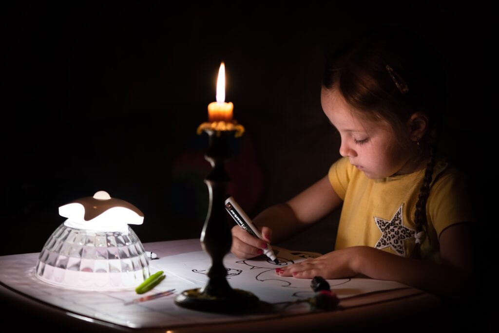 Girl draws by candlelight in a dark room.